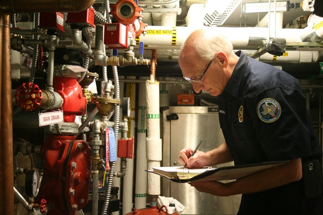 Fire Marshal inspecting red fire suppression pipes in a boiler room.